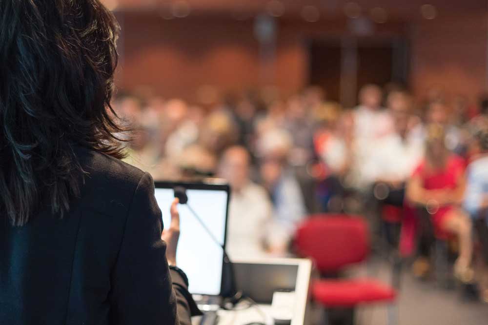 rear view of business woman at lectern lecturing at conference