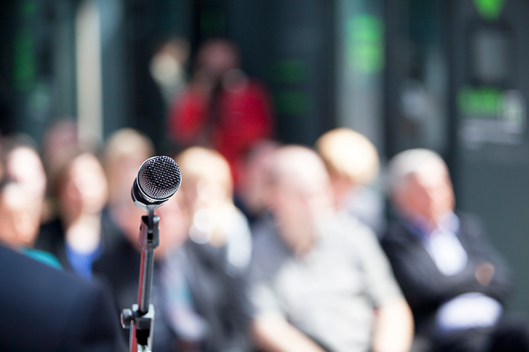 Photo of a microphone in front of an audience